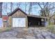 View of garage featuring white door and adjacent shed, set amongst bare trees and concrete flooring at 110 E Hendricks St, Shelbyville, IN 46176