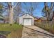 Detached single-car garage with white siding and a concrete driveway surrounded by mature trees and landscaping at 136 W 43Rd St, Indianapolis, IN 46208