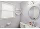 Well-lit powder room with a round mirror, window, toilet, and white vanity with decorative shelves at 1710 Bittersweet Dr, Anderson, IN 46011