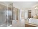 Bright bathroom featuring a soaking tub, glass enclosed shower, neutral tile, and access to the walk-in closet at 3892 Pelham Rd, Carmel, IN 46074