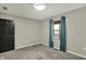 A minimalist bedroom with neutral walls, carpet flooring, a black door, and a single window dressed with blue curtains at 7023 Mustang Ct, Martinsville, IN 46151