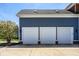 Three-car garage featuring traditional white doors and blue siding, complemented by lush landscaping at 12897 Queens Troop, Carmel, IN 46032