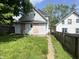 View of the backyard and exterior of a home, with an overgrown lawn and boarded up windows at 2148 Singleton St, Indianapolis, IN 46203