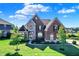 Imposing two-story brick home featuring a manicured lawn, arched windows, and stone accents under a partly cloudy sky at 3715 Kendall Wood Dr, Carmel, IN 46032