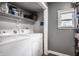 A functional laundry room features a side-by-side washer and dryer, complemented by convenient shelving and a bright window at 902 Villa Ave, Indianapolis, IN 46203