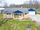 Quaint one story home with blue trim, a detached garage, and inviting front porch with chairs at 7212 E Rocklane Rd, Needham, IN 46162