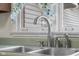 Close-up of a kitchen sink with chrome fixtures, including a sprayer, under a window with patterned curtains at 6141 Madison Ave, Indianapolis, IN 46227