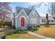View of charming gray home with a red arched entry door, gray roof, and traditional lawn with spring color at 2309 Pearl St, Columbus, IN 47201