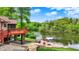 Backyard view of a home with access to a lake, featuring a stone patio, a wooden deck, and mature trees at 5571 Poff Rd, Martinsville, IN 46151