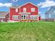 View of a two-story home with red siding, large backyard with grass and patio area at 10603 Hinterland Dr, Fishers, IN 46038