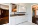A well-lit wet bar with marble floors, white cabinets, and a stainless steel sink adjacent to rooms with wood flooring at 6047 W 56Th St, Indianapolis, IN 46254