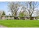 A single-story home with a stone facade and green shutters sits behind a green lawn and mature trees at 7575 Holliday W Dr, Indianapolis, IN 46260