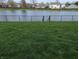 Lush backyard with green lawn, a fenced pond, and mature trees in the distance at 561 Prince Dr, Greenwood, IN 46142