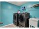 A vibrant laundry room features modern washer, dryer, utility sink, wire rack, and blue walls at 7736 Eagle Point Cir, Zionsville, IN 46077