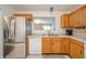 Open kitchen with stainless steel refrigerator, view to the living room, and wood cabinets at 12319 Wolf Run Rd, Noblesville, IN 46060