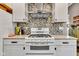 Close-up of a stove in a well-lit kitchen featuring white cabinets, granite countertops, and a mosaic backsplash at 524 N Meridian St, Lebanon, IN 46052