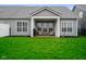 A gray home's backyard features a lush green lawn and a covered porch with patio furniture at 8160 Nik St, Brownsburg, IN 46112