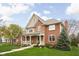 Inviting two-story brick home with a covered front porch and lush green lawn and mature tree at 4777 Madras Ct, Zionsville, IN 46077