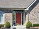 Close up of the front door featuring sidelights, a red door and decorative shrubbery at 8717 Vintner Ct, Indianapolis, IN 46256