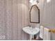 Charming powder room with pedestal sink, decorative mirror, and patterned wallpaper at 958 Tamarack Cir N Dr, Indianapolis, IN 46260