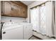Bright laundry room with a washer, dryer, upper cabinets and window with white curtains at 3753 Whippoorwill Lake S Dr, Monrovia, IN 46157