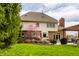 Home's back exterior showcases a covered patio, outdoor seating, lush greenery, and blossoming tree at 7326 Elm Ridge Dr, Indianapolis, IN 46236