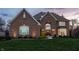 Beautiful brick home with landscape lighting, a well-kept lawn, and manicured shrubbery at dusk at 7326 Elm Ridge Dr, Indianapolis, IN 46236