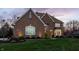 Elegant brick home with a well-kept lawn, manicured landscaping, and warm lighting at dusk at 7326 Elm Ridge Dr, Indianapolis, IN 46236