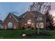 Well-lit brick home with a manicured lawn, elegant landscaping, and a peaceful evening sky at 7326 Elm Ridge Dr, Indianapolis, IN 46236
