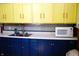 Bright kitchen featuring yellow upper cabinets, blue lower cabinets, stainless sink and patterned backsplash at 2025 Barth Ave, Indianapolis, IN 46203