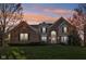 Charming two-story brick home with an arched entryway, manicured lawn, and mature trees under a vibrant sunset at 8965 Snowberry Ct, Zionsville, IN 46077