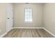 An empty bedroom featuring wood-look floors, light tan walls, a window, and a white door at 8560 N College Ave, Indianapolis, IN 46240