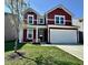 Charming two-story home featuring vibrant red siding, white trim, a well-manicured lawn, and an attached two-car garage at 1380 Delacorte Cir, Shelbyville, IN 46176