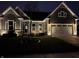 Night view of a beautifully lit home featuring stone accents, a two-car garage, and landscaped yard at 13494 Moorcroft Dr, Fishers, IN 46037