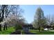 A long driveway leads to a charming two-story brick home with an attached garage, framed by flowering trees and a green lawn at 3790 E Pleasant Run Parkway North Dr, Indianapolis, IN 46201