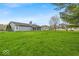 Lush green backyard featuring manicured lawn, trees, and screened in patio at 9328 Haddington W Dr, Indianapolis, IN 46256