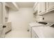 Well-lit laundry room with modern washer and dryer, cabinets, sink, and neutral tile flooring at 9435 Tamarack Dr # 94, Indianapolis, IN 46260