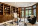 This office features wooden bookshelves, a glass desk, a comfortable chair, and large windows overlooking the yard at 9435 Tamarack Dr # 94, Indianapolis, IN 46260