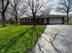 Quaint single-story brick home with a lush green lawn, mature trees, and a storage shed at 7002 Mclain Dr, Indianapolis, IN 46217