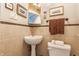 Cozy powder room featuring a pedestal sink, decorative mirror, neutral tile, and convenient toilet at 4451 N Washington Blvd, Indianapolis, IN 46205