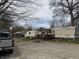 Exterior view of a mobile home, featuring a covered porch, a spacious dirt yard, and mature trees at 154 Tippecanoe Dr, Noblesville, IN 46062