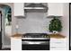 Close-up of kitchen gas range with stainless steel hood, mosaic backsplash, and warm wood countertops at 1646 Fisher Ave, Indianapolis, IN 46224