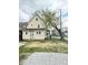 View of the two-story home with yellow siding, large yard and detached gravel parking space at 3502 N Illinois St, Indianapolis, IN 46208