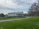 View of a large modern white outbuilding with black trim, metal roof, and a covered patio, set back from a long driveway at 4560 S 975 E, Zionsville, IN 46077