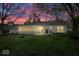 Back exterior of house with sunroom, a green yard, and fire pit as the sun is setting at 7709 Lewis Rd, Indianapolis, IN 46256
