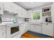 Well-lit kitchen with white appliances, cabinets, and a farmhouse sink, complemented by hardwood floors and a window view at 7709 Lewis Rd, Indianapolis, IN 46256