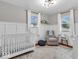 Cozy Bedroom with white crib, rocker, wainscoting, modern ceiling fixture and windows providing natural light at 8621 Manderley Dr, Indianapolis, IN 46240