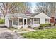 Quaint home boasts an enclosed porch, large windows, and is surrounded by blossoming trees and a green lawn at 6153 Evanston Ave, Indianapolis, IN 46220