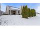 Back exterior view featuring covered patio, neat evergreens, and snow-covered yard at 6586 W Winding Bnd, McCordsville, IN 46055