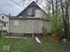 Rear exterior view of a distressed property showing siding damage, boarded windows and overgrown weeds at 727 W 25Th St, Indianapolis, IN 46208